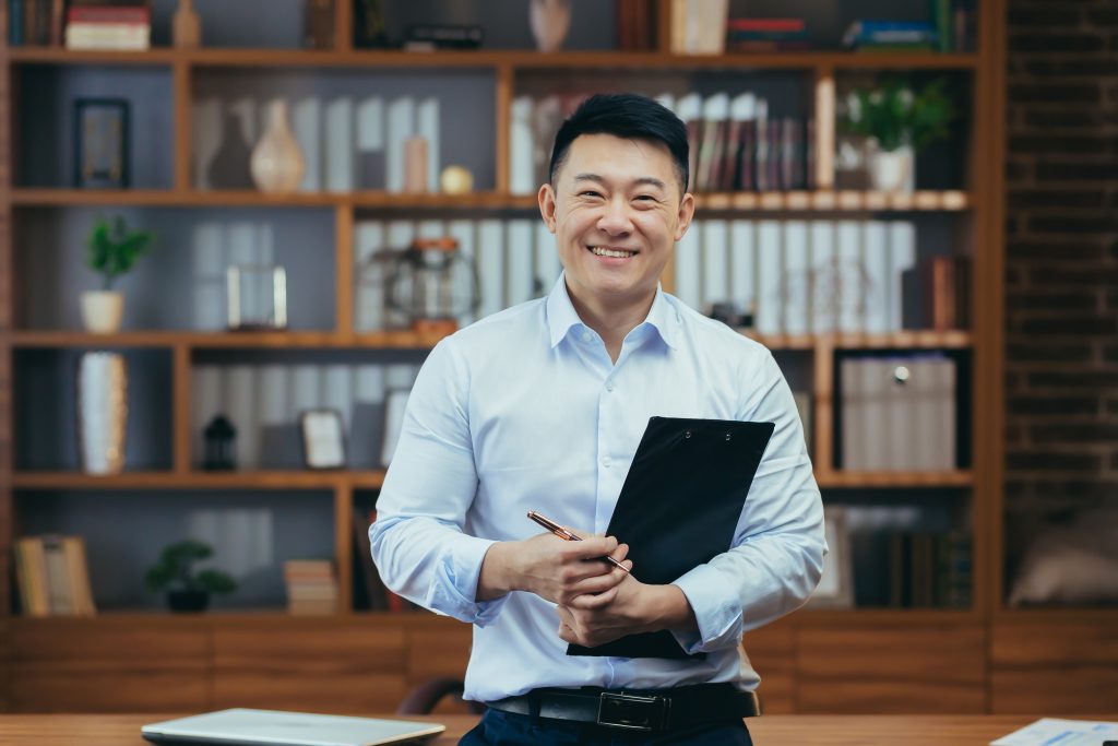 Portrait of a successful Asian teacher, a man in a shirt looking at the camera and smiling, in the classic office of the university director