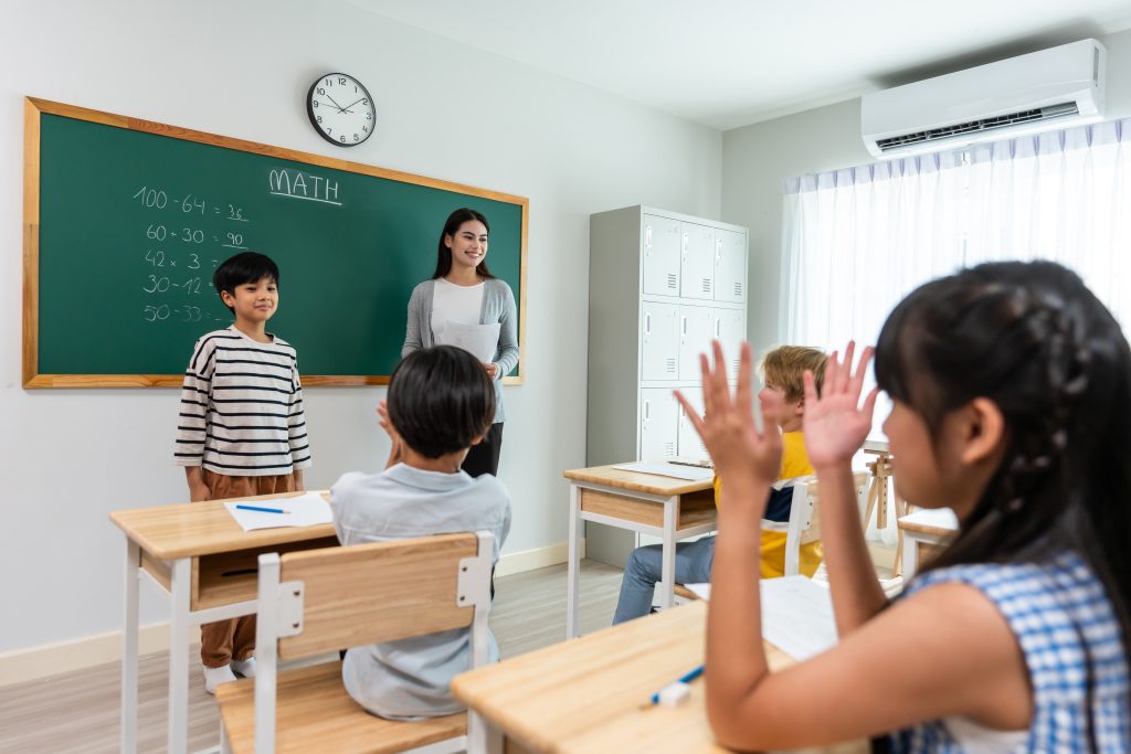 Group of student learn with teacher in classroom at elementary school. Attractive beautiful female instructor master explain and educate young children with happiness and fun activity at kindergarten.