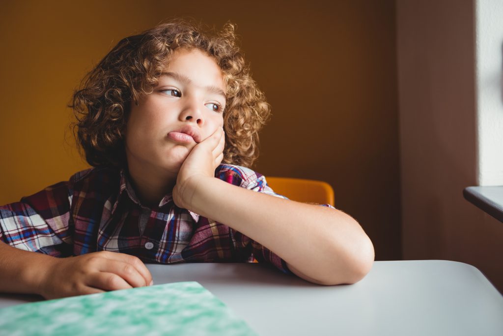 Boy sitting down on his chair and dreaming at school