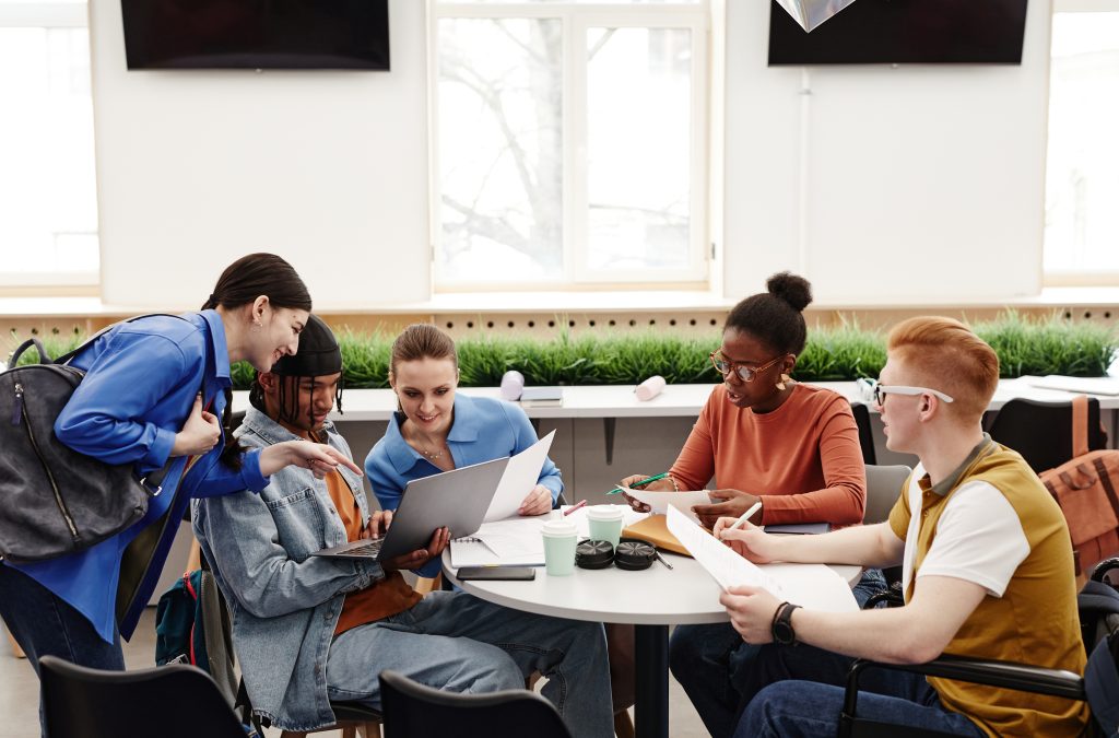 Diverse group of college students studying together at round table and discussing project, copy space