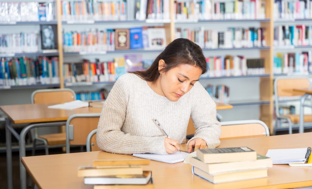 Portrait of young adult woman studying in at public library