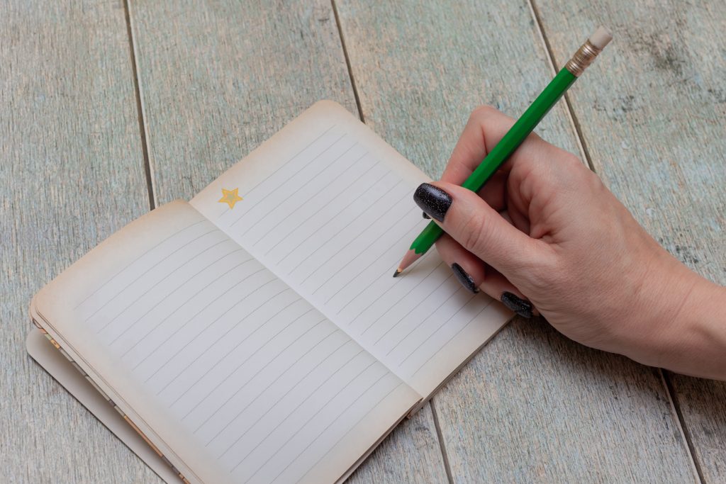 female hand writes with a pencil in a notebook