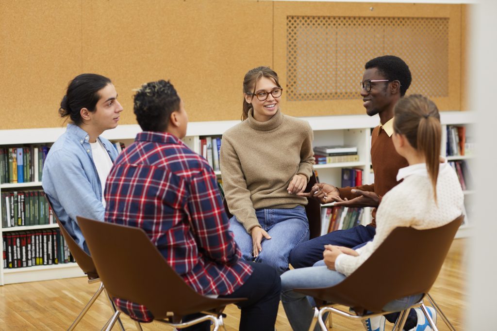 Multi-ethnic group of young people sitting in circle and sharing ideas during class in college, copy space