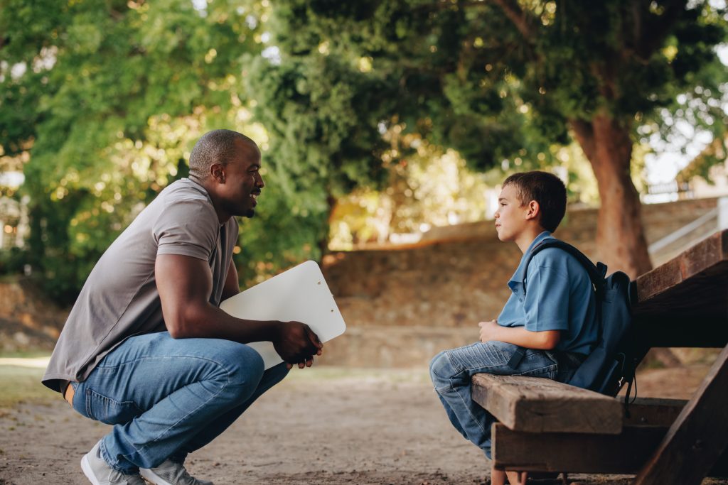 Mentor talking to a young school kid outside class. Primary school teacher motivating a young boy. Teacher providing support and encouragement for a pupil in elementary school.