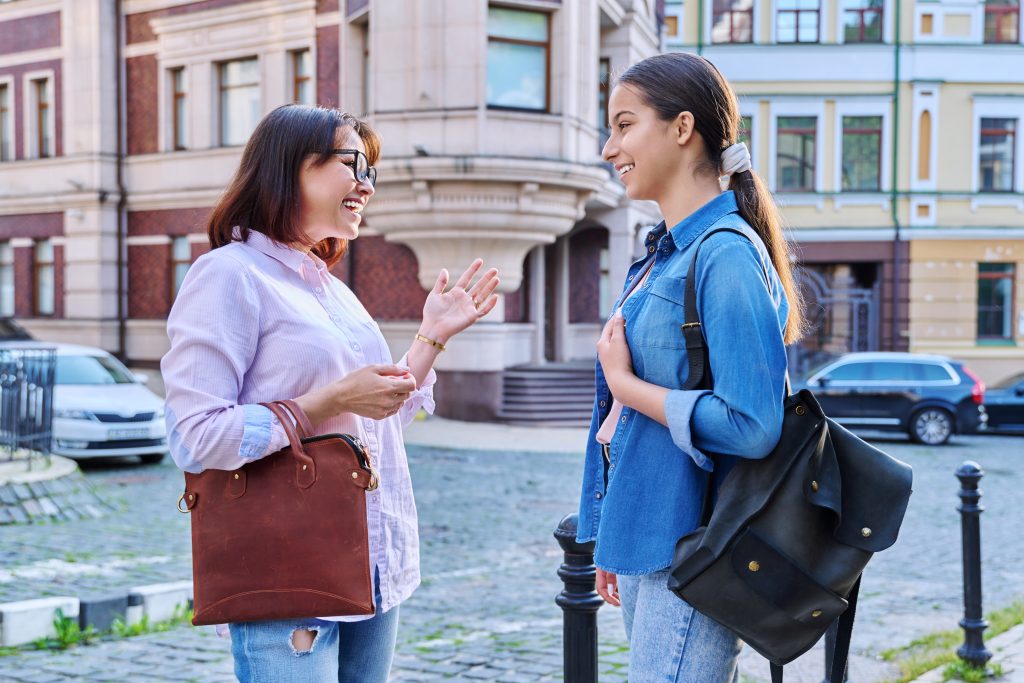 Talking mom and teenage daughter outdoors, on a city street. Parents and child teenager laughing, smiling, walking together. Family, two generations, lifestyle, leisure, people concept