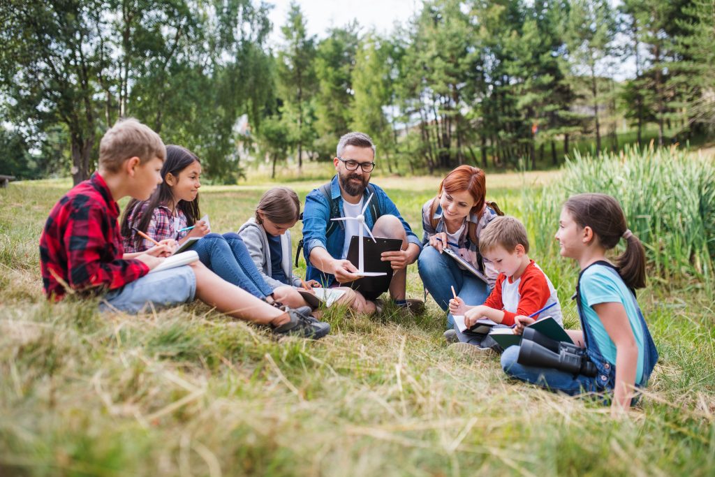 A group of school children with teacher and windmill model on field trip in nature.