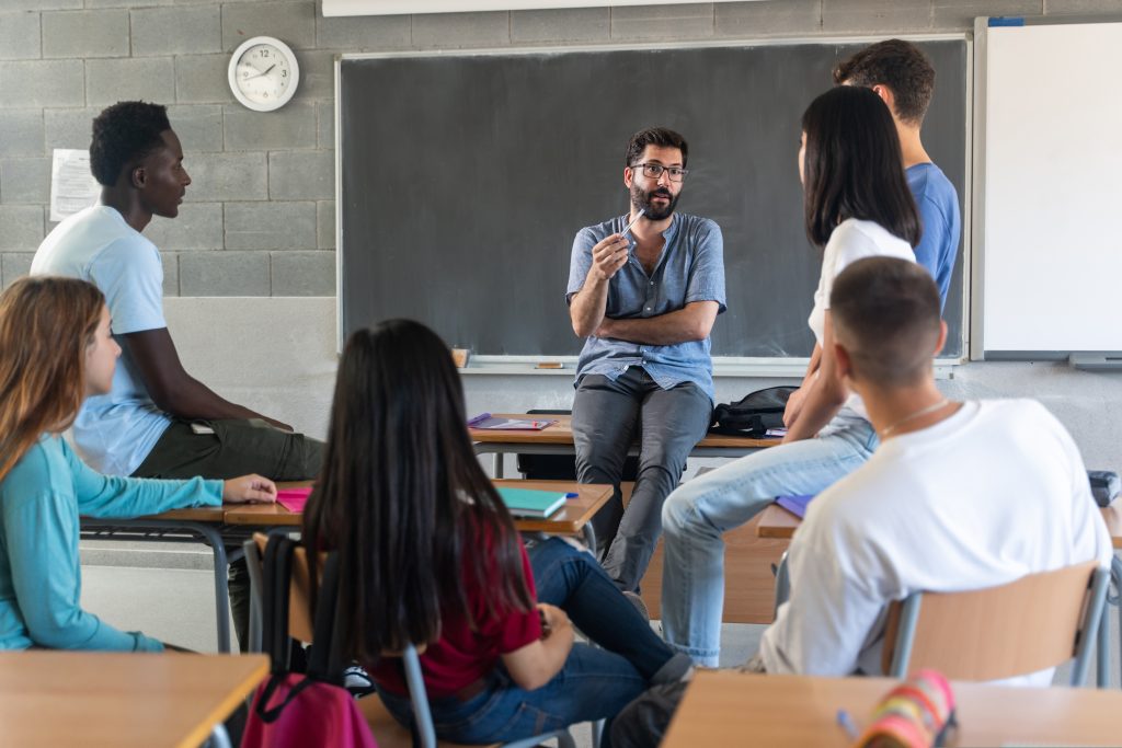 Young teacher talking with teenager students seating in a circle at school