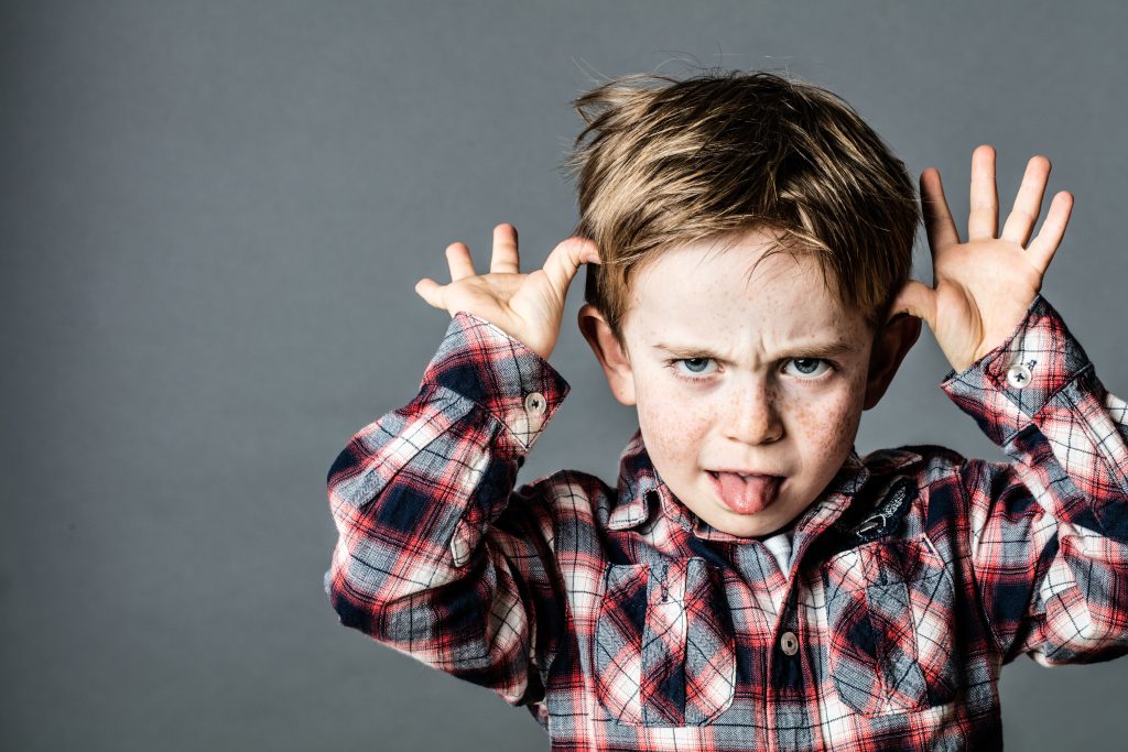 angry little brat enjoying making a grimace, sticking out his tongue, playing with his hands for  misbehavior, contrast effects, grey background