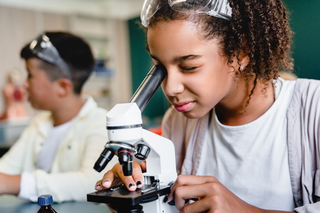 African-american schoolgirl pupil student using working with microscope at biology chemistry lesson class at school lab. Science lesson concept