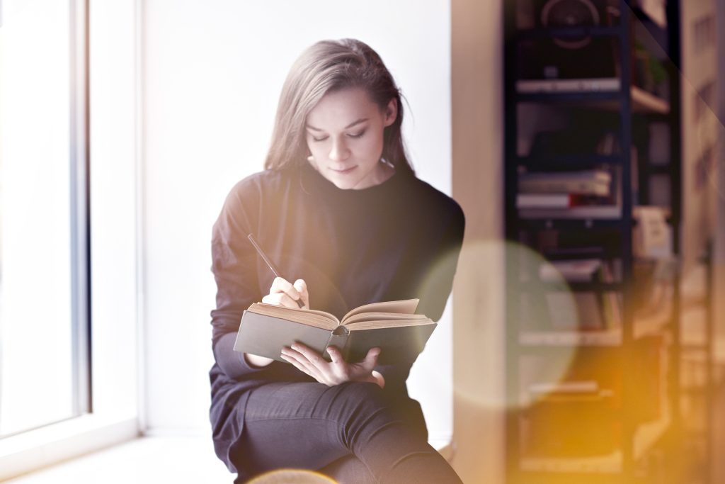 Young brunette woman with a book in a public library. Sitting near window