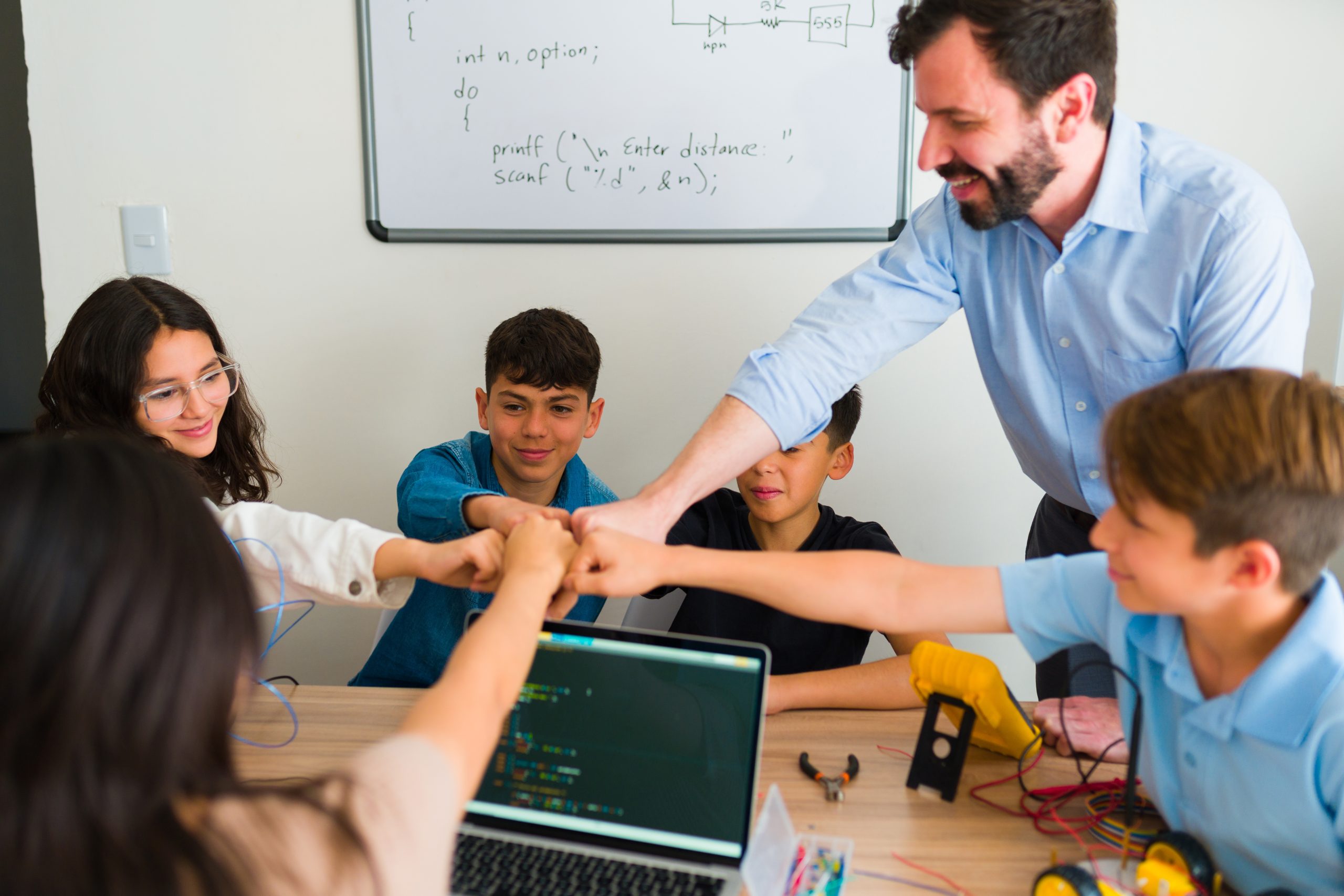 Group of teen students and teacher getting ready or celebrating doing a robotic collaborative project during their coding class