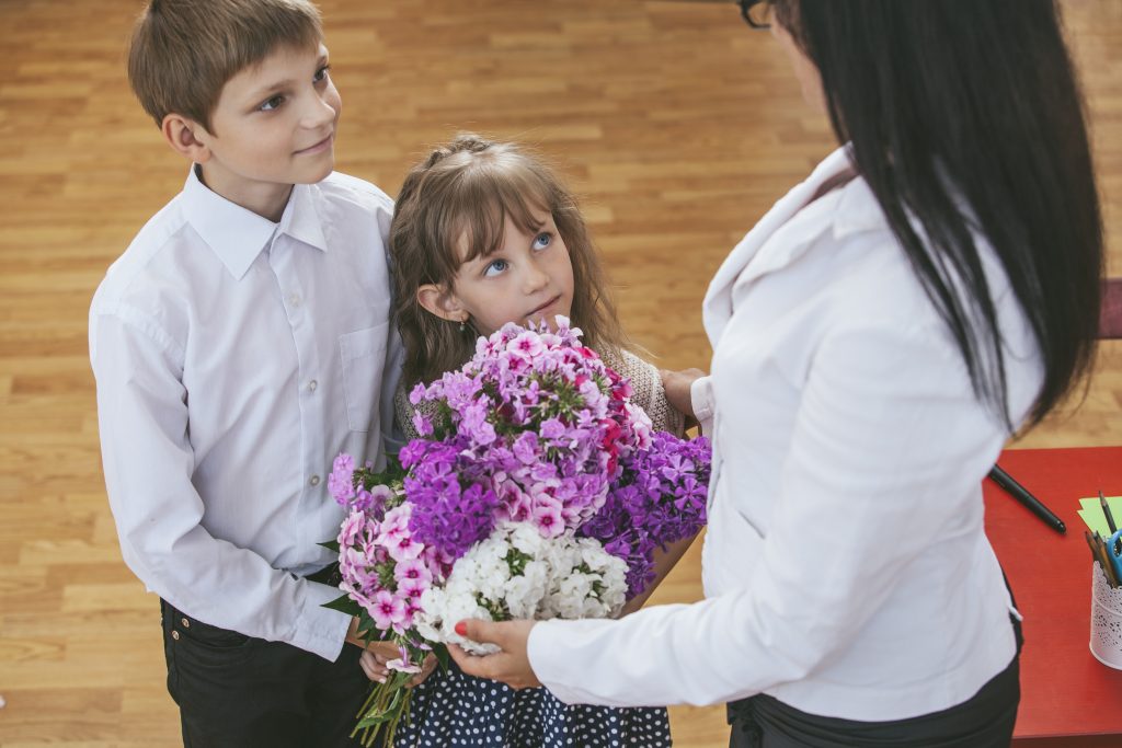 Boy and girl children give flowers as a school teacher in teache