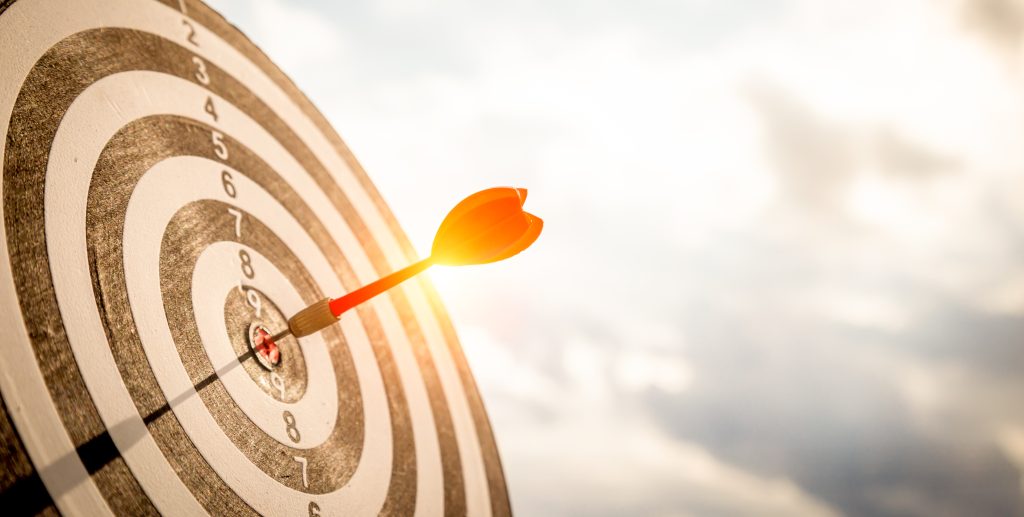 Close up shot red darts arrows in the target  of dartboard center on dark blue sky background. Business target or goal success and winner concept.