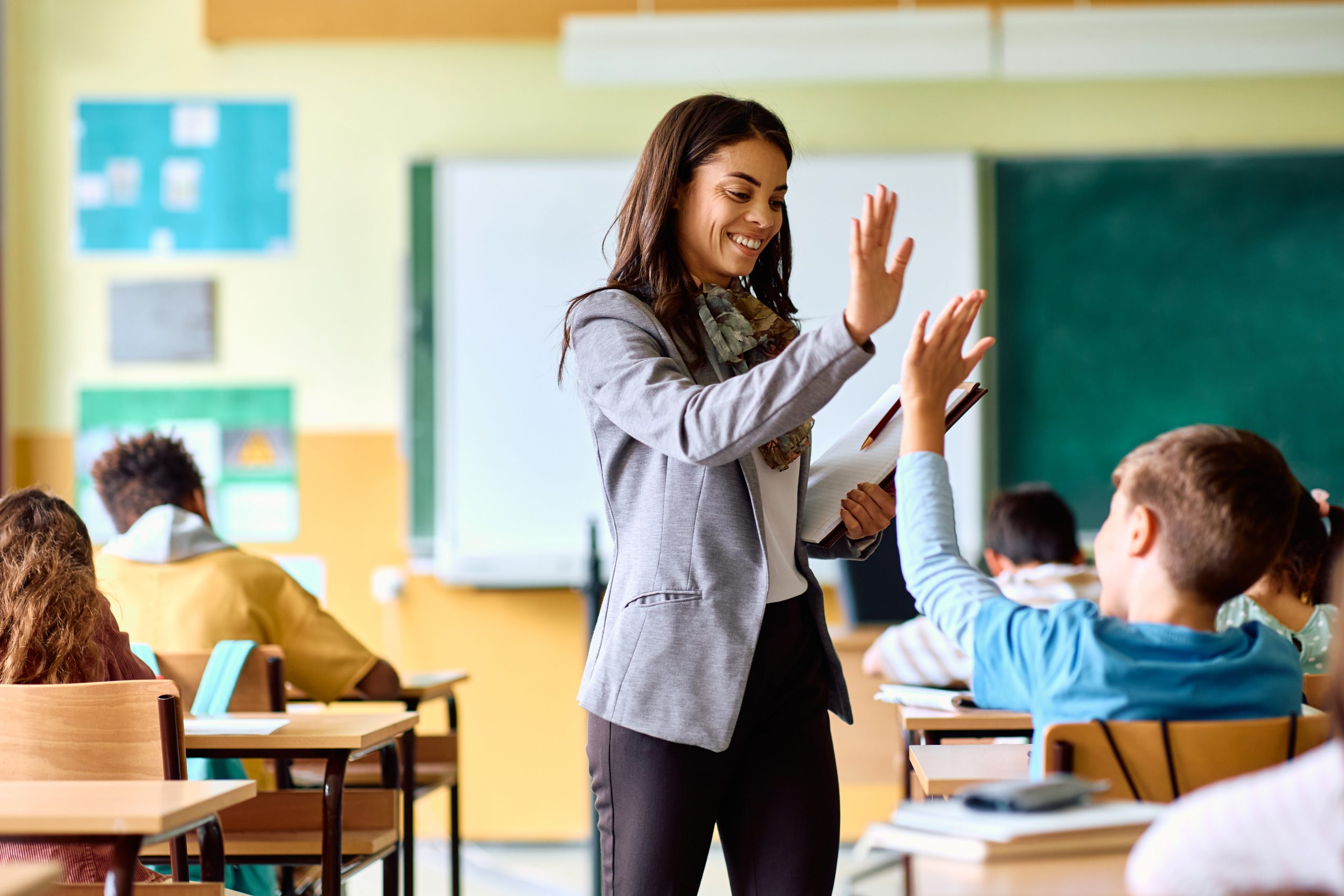 Happy Hispanic teacher and schoolboy giving high five during class at school.