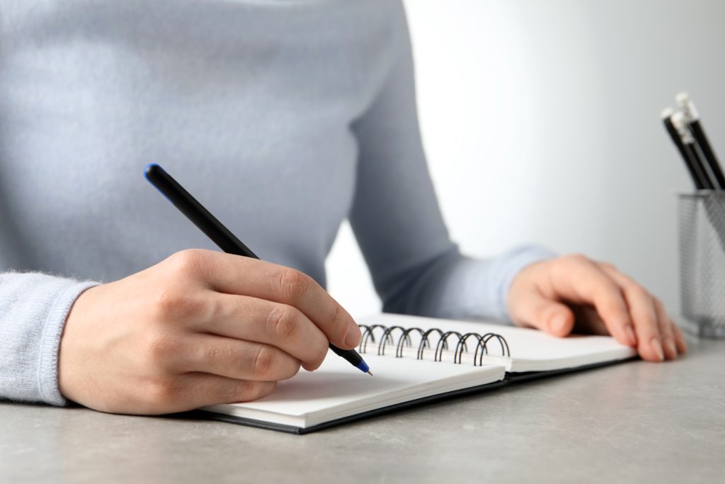Woman with pen and notepad at grey table, closeup