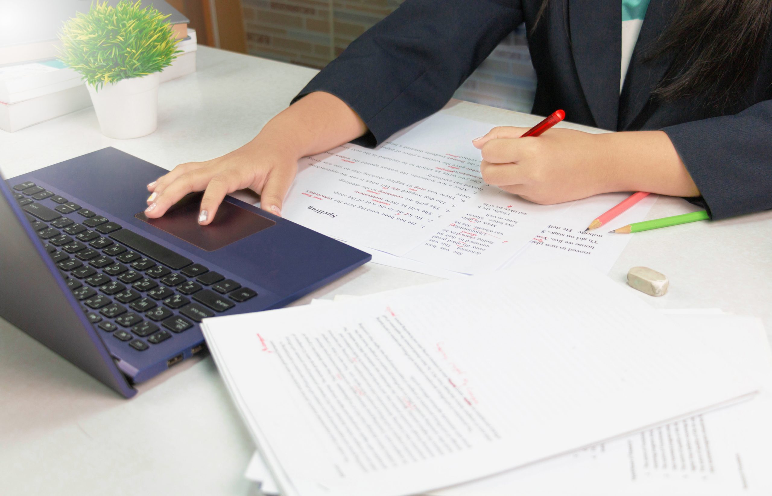 hand holding red pen over proofreading paper on white table