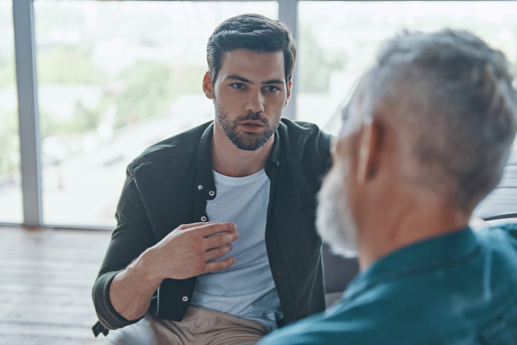 Handsome young man talking to his senior father while spending time at home together