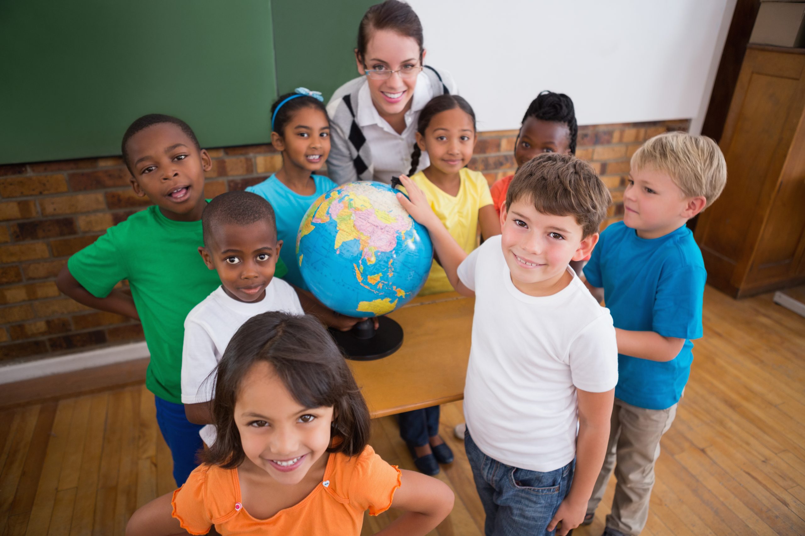 Cute pupils pointing to globe in classroom at the elementary school