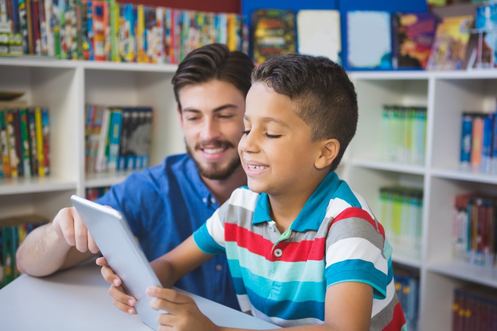 Teacher and school kid using digital table in library at school