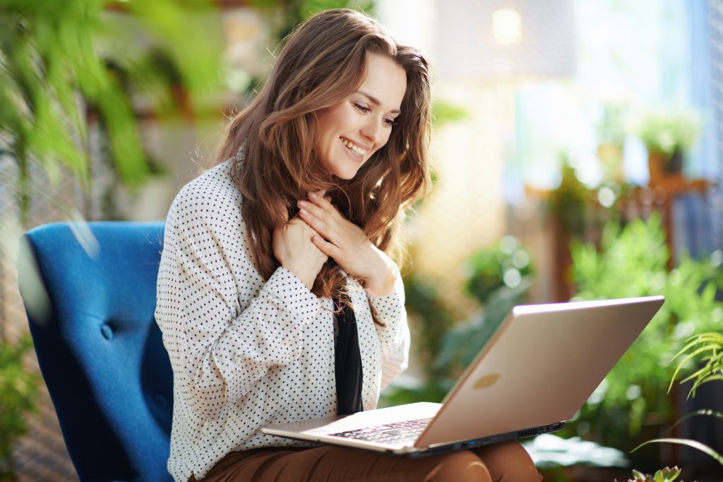 Green Home. happy young woman with long wavy hair in the modern house in sunny day having online meeting on a laptop.