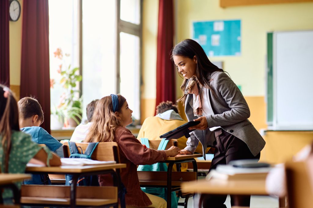 Happy elementary student communicating with her teacher during a class at school.