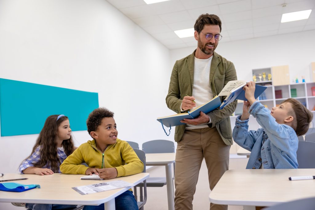 Smiling man teacher in classroom with little students.