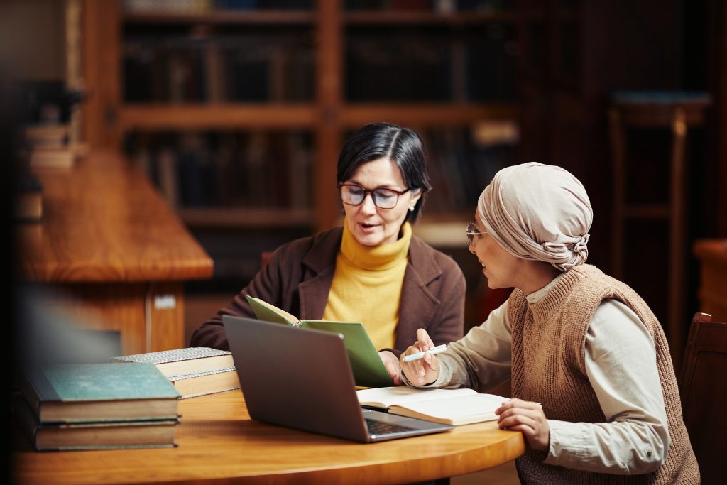 Warm toned portrait of two adult women studying together in classic college library, copy space