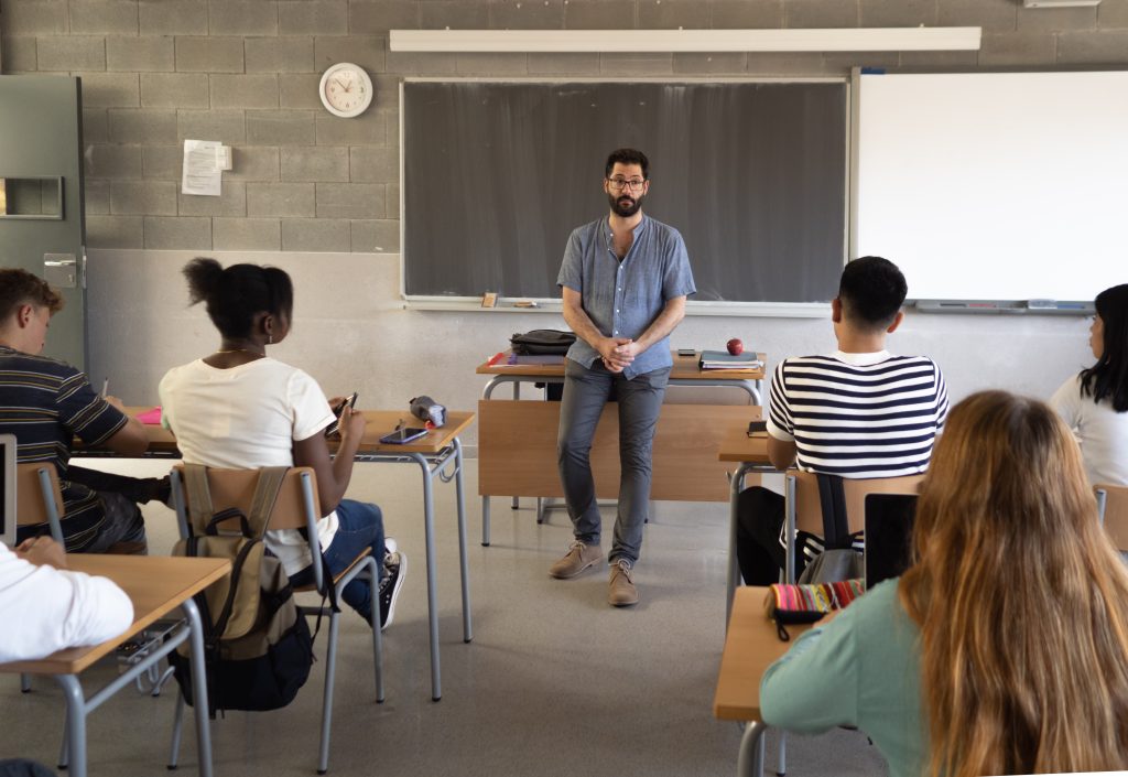 Male teacher explaining the class lesson in a classroom with multi-ethnic students. Education in diversity, back to school, High school