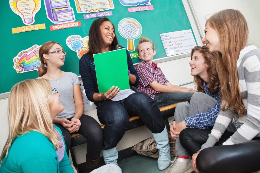 Happy teacher About To Read To Her Classroom Full Of Students Sitting In A Circle.