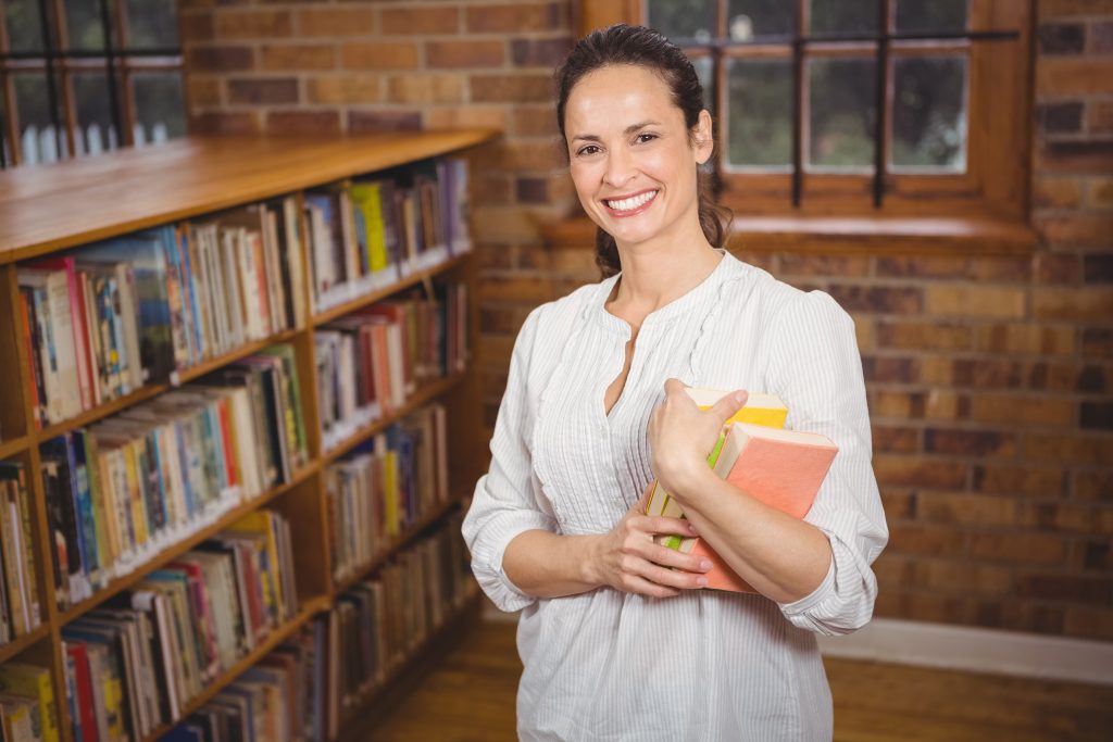 Smiling teacher holding books in her hands at the elementary school