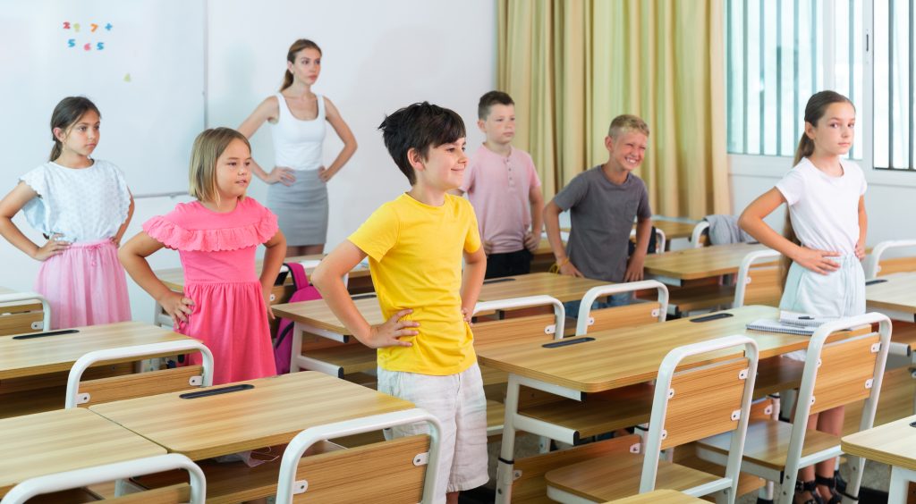 Schoolchildren with teacher performing physical exercises in classroom in elementary school