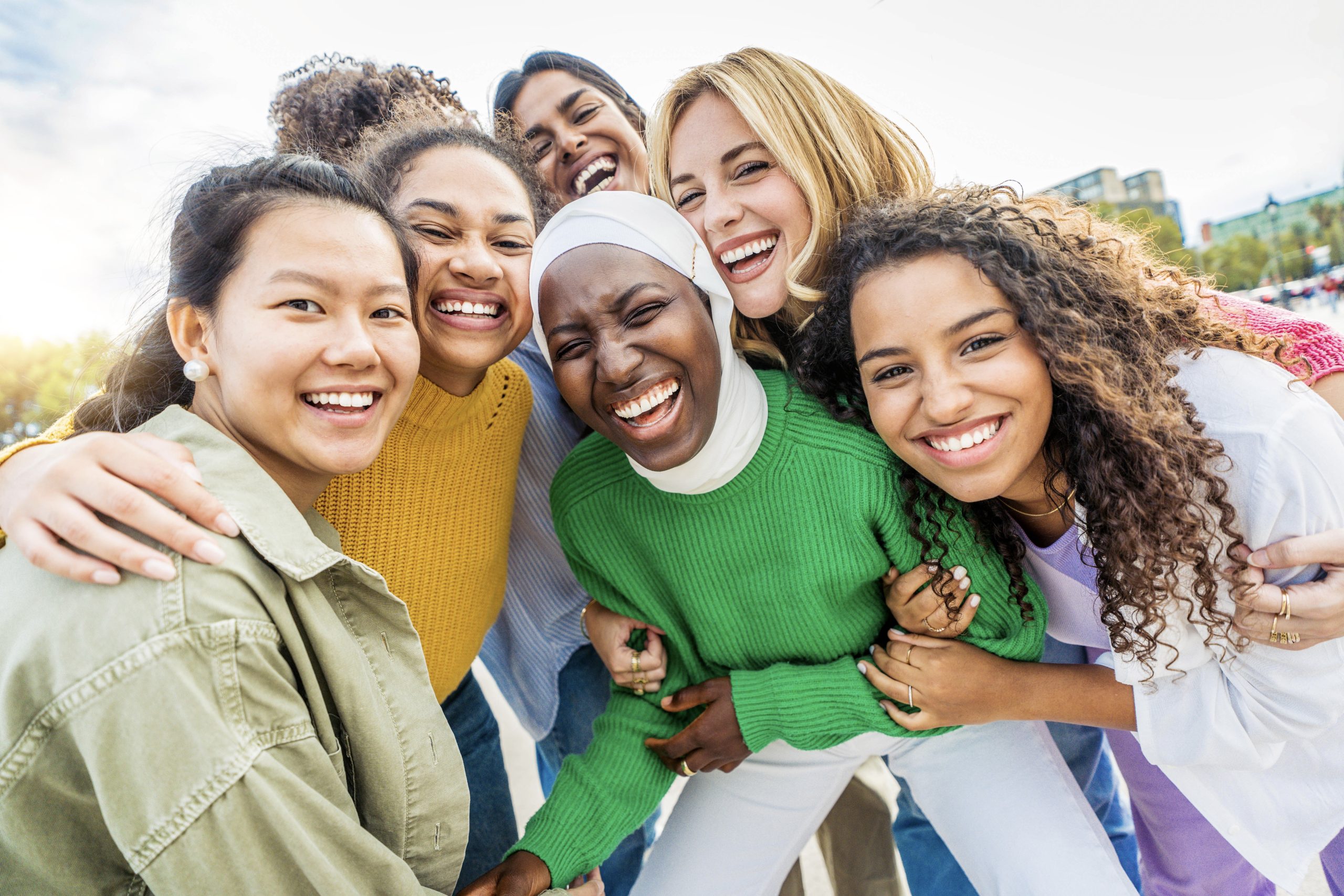 Multi ethnic group of young women hugging outside - Happy girlsfriends having fun laughing out loud on city street - Female community concept with cheerful girls standing together - Women  power